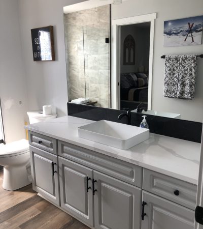A beautiful but simple remodeled bathroom with a wide mirror and white cabinets